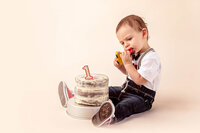 one year old sitting beside birthday cake holding small toy car