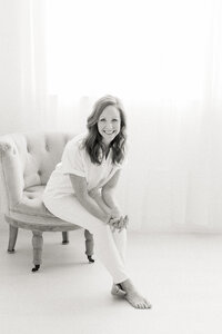 Black and white professional headshot of a Dallas TX business owner posing for her branding session as she sits on a chair in a photography studio.