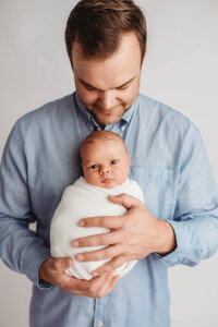 Newborn Pictures in Charleston - Father embraces her newborn baby during Newborn Pictures at Holy City Babies Newborn Photography Studio in Charleston, SC.
