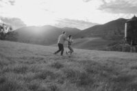 couple playing tag engagement photos in open field by water tower and mountain in bay area california