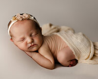 Sleeping newborn baby wearing a delicate floral headband and posed on a neutral blanket during a studio session with newborn photographer Kaitlyn Dawn Photography.
