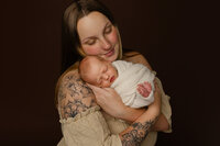 Mother holding her newborn baby wrapped in cream fabric. Photographed by Inland Empire newborn photographer Kaitlyn Dawn Photography.