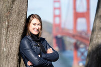 Woman leaning against a tree while wearing a black leather jacket in front of the golden gate bridge