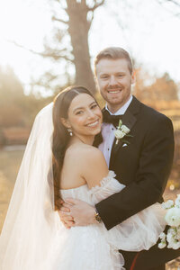 bride and groom embrace smiling at the camera