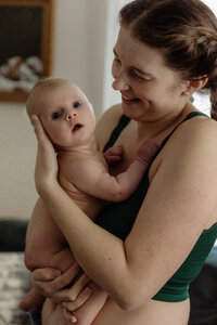 A newborn is gently cradled by mom in a New Englnad home. Fine art lifestyle family photography by Damini Photography