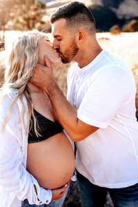Maternity Photographer, a man kisses his pregnant wife near the beach