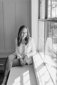 Beautiful black and white professional headshot photo of a Dallas Texas business woman posing by a window smiling at the camera for her branding/headshot session.