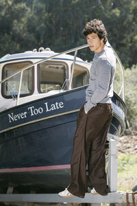 Grey knit top and brown wide-leg trousers photographed against a moored fishing boat