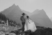 A wedding couple poses in front of a mountain overlook in Glacier National Park.