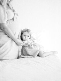 A toddler daughter with her ear against mom's pregnant belly, trying to hear her baby sister.