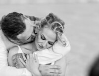 St. Augustine Beach, wedding capturing a bride and groom in a close embrace in a black and white, the groom kissing her neck as wind lifts her hair. - A portrait experience by Nature's Child Photography.