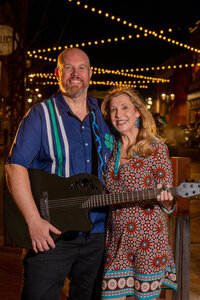 Two people smiling together while one holds a guitar
