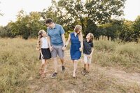 A family of four strolls hand in hand through High Park's grassy fields, with the warm glow of a sunset casting a golden hue over the trees in the background—perfect for capturing timeless Toronto family photography.