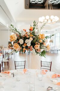 A bouquet of orange, yellow and dust rose flowers sit at the center of each dining table.