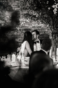Authentic documentary moment of a bride and groom kissing at a candlelit reception table at the Wythe Hotel in Brooklyn.