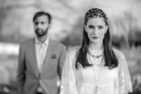 Black and white portrait of a couple outdoors, the man in a light suit, the woman in white with braided hair.