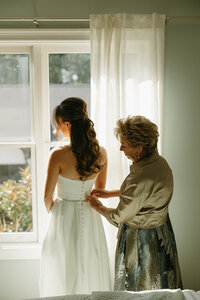 mother of the bride helping bride into wedding gown