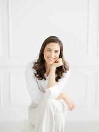 Beautiful in studio headshot photo of a Dallas small business owner sitting on a stool and looking at the photographer smiling.
