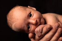 A close up picture of a newborn baby in her father's hands. Her whole hand is wrapped around his index finger.
