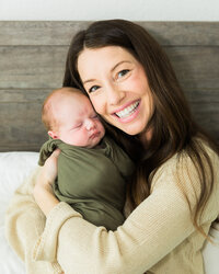 Smiling mother holding her sleeping swaddled newborn baby during an in-home lifestyle newborn photography session.
