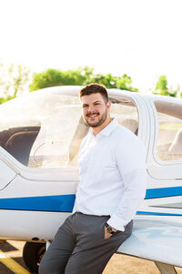 Senior male wearing a suite standing beside an airplane at the MTSU aviation college