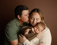 Parents embracing their newborn baby while sharing a kiss during a studio newborn family portrait session by Inland Empire newborn photographer Kaitlyn Dawn Photography.
