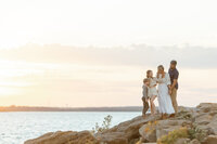 A beautiful family sunset photo as they are posing on rocks holding each other at a local DFW lake for their photographer.