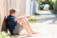 senior boy sitting against a wooden fence and looking away from the camera.
