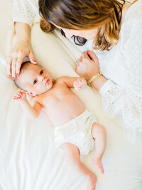Mother smiling down at her newborn baby lying on a bed during a relaxed in-home newborn photography session.