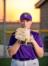 Professional photography by Nature's Child Photography: Tween girl in a purple softball uniform holding her glove up with a focused expression during a sports session in O’Fallon, Illinois.
