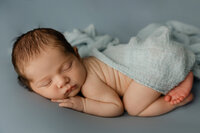 Sleeping newborn baby boy posed on a soft blue blanket with hands under chin during a professional newborn photography session by Kaitlyn Dawn Photography.