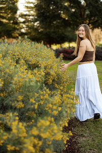 High school senior girl standing among yellow flowers during golden hour, outdoor senior portrait by Kaitlyn Dawn Photography.