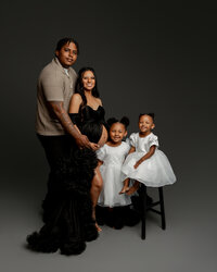 Family maternity portrait with parents and two young daughters wearing white dresses during a studio pregnancy photography session by Kaitlyn Dawn Photography.