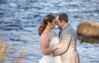 Bride and groom holding each other beside a mountain lake during a wedding photography session in Graeagle, California with Nature’s Child Photography, soft evening light reflecting across the water as the couple shares a quiet moment together.