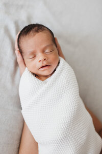 Sleeping newborn baby boy who is laying in his dads large hands. Captured by Toronto Newborn Photographer Claire Binks