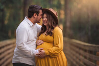 Expecting couple embracing on wooden bridge during golden hour maternity photography session