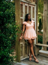 Senior portrait at Bella Sera Gardens in Loxley, Alabama — standing by wooden shutters in a
pink dress, looking off into the distance.