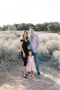 The Parker family posing together in a natural desert landscape in Las Vegas, with parents and their young daughter smiling in soft light during an outdoor family portrait session.