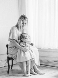 Toddler embracing her pregnant mom who is sitting on a chair