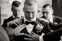 A documentary wedding photography shot of a groom being helped by his groomsmen, focusing on the genuine connection of the wedding party.