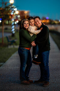 Parents standing with their young son on a walkway at night during a New Bern family session