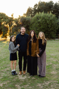 Father and mother standing with two teenage daughters in a park at sunset, coordinated neutral outfits captured by Kaitlyn Dawn Photography, professional family portrait photographer.