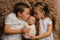 Older siblings holding their newborn baby and smiling. Photographed by Inland Empire newborn photographer Kaitlyn Dawn Photography.