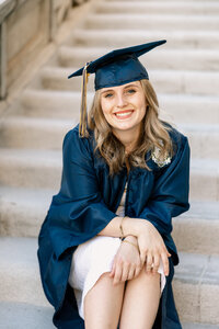 High school graduate wearing a cap and gown sitting on stone steps, graduation portrait captured by Kaitlyn Dawn Photography.