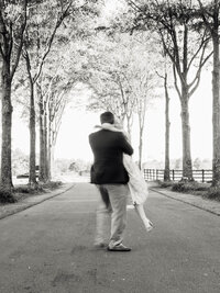 A high-contrast black and white shot of a groom lifting the bride, capturing a real moment of joy with a natural motion blur.