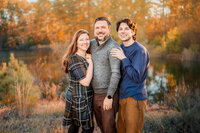 Smiling family photographed near a wooded lake during outdoor family session in Eastern North Carolina
