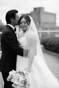 Groom kisses the bride gently on the cheek while she holds her bouqet