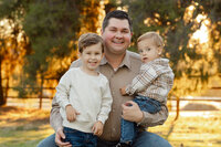 Father sitting and holding his two young sons in warm golden light, natural candid family portrait by Kaitlyn Dawn Photography, lifestyle family photography specialist.
