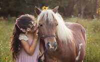 Professional photography by Nature's Child Photography: Young girl in a floral crown and soft pink gown shares a quiet moment with a pony during a Fernadina Beach signature.Princess session.