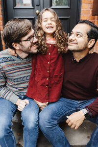 two dads and their daughter sitting on the steps of their Toronto home